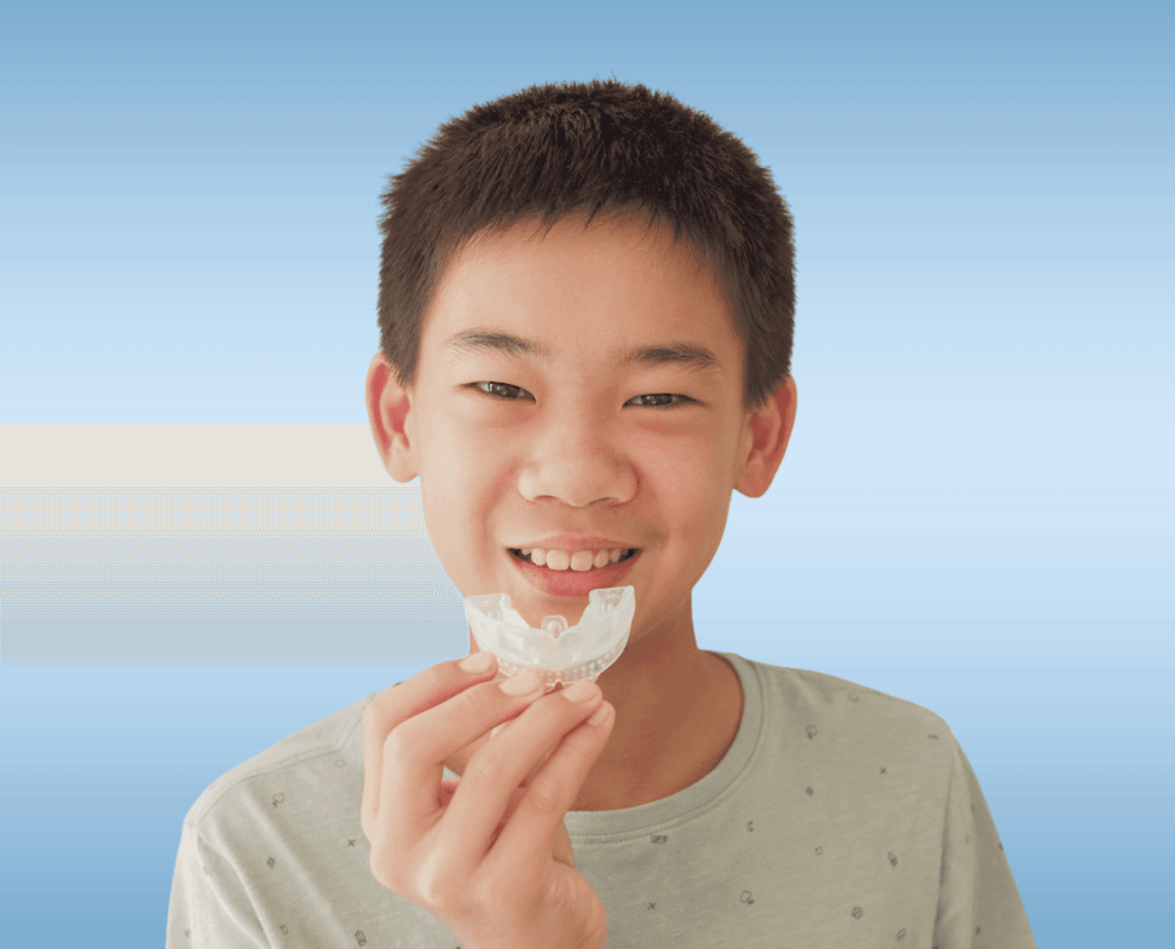 Young boy smiling while holding a custom mouthguard